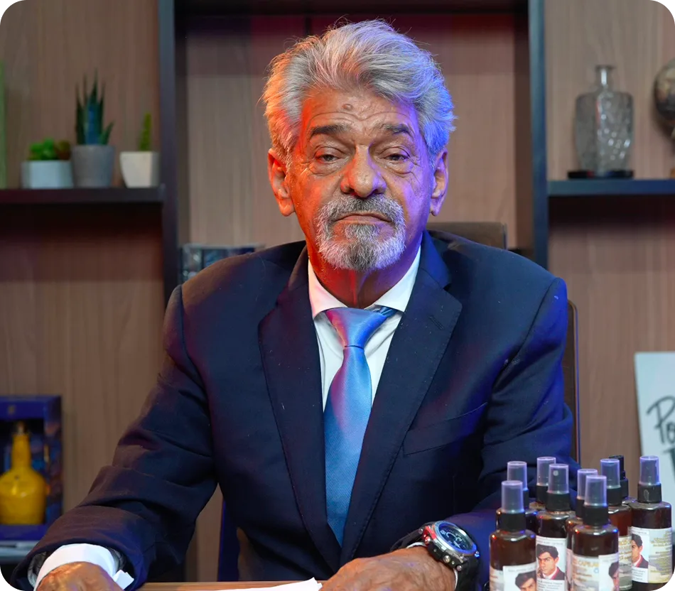 Walter Silva, criador do tônico capilar, sentado em seu escritório com os frascos do produto